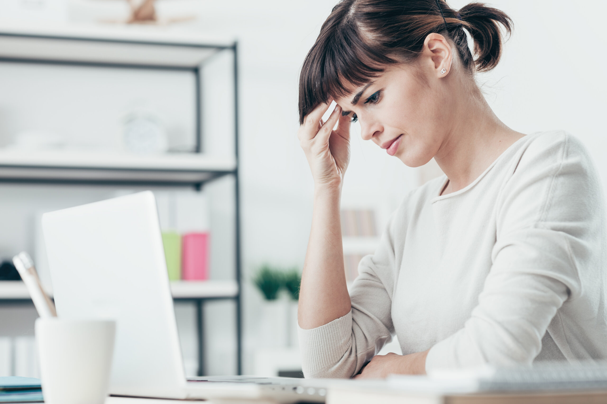 Tired woman having a bad headache, she is sitting at office desk and touching her temple