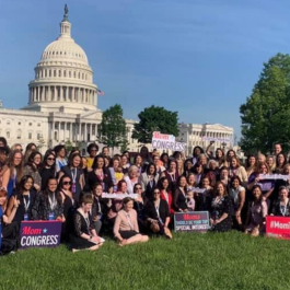 Women gathered in front of the US Capitol building holding Mom Congress signs