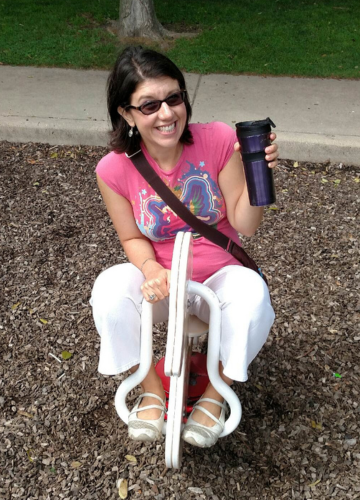 Valerie on the playground holding a purple travel coffee mug and wearing a pink unicorn t-shirt