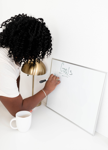 Black woman writing "Goals" on a white board